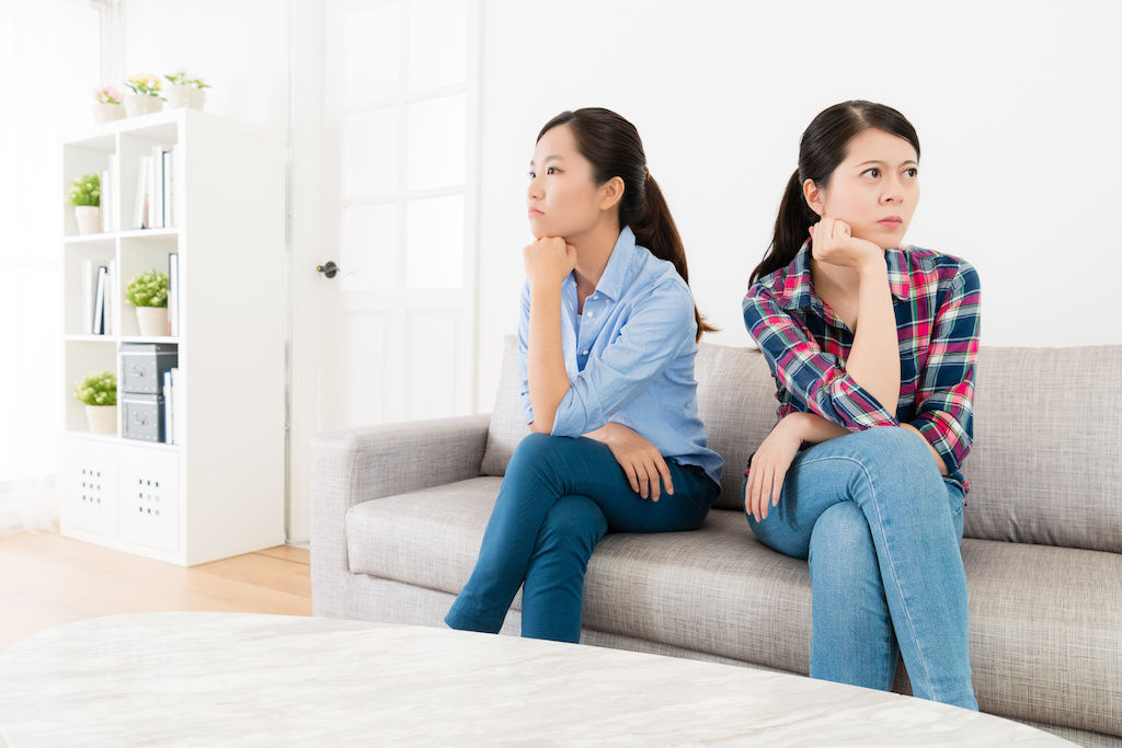 Two roommates sitting on couch with backs turned to each other